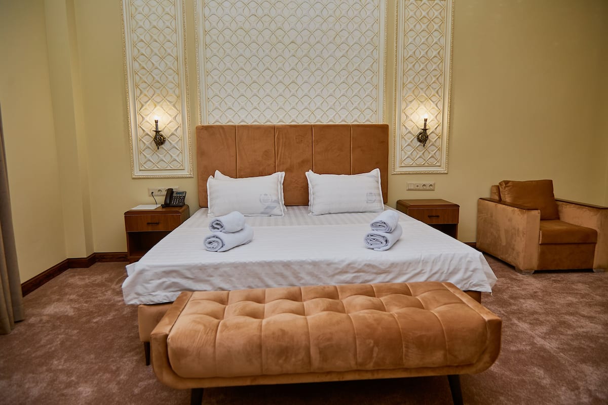 A hotel room with a large bed, two bedside tables, a chair, and a bench.