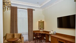 A hotel room with a sofa, a desk, a chair, a television, and a window with curtains. - Sangzor Boutique Hotel (Samarkand)
