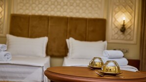 A hotel room with two beds, a round wooden table with a glass dome centerpiece, and a wall-mounted light fixture. - Sangzor Boutique Hotel (Samarkand)