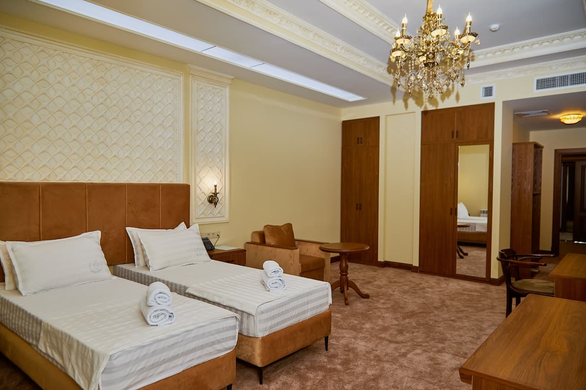 A hotel room with two beds, a chandelier, a small table, and a seating area.