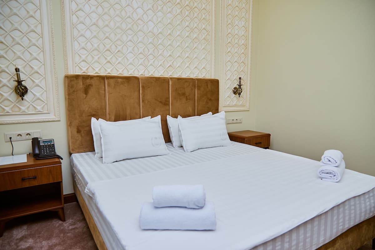 A neatly made bed with white linens, a wooden nightstand with a telephone, and a wall with decorative paneling.