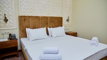A neatly made bed with white linens, a wooden nightstand with a telephone, and a wall with decorative paneling.