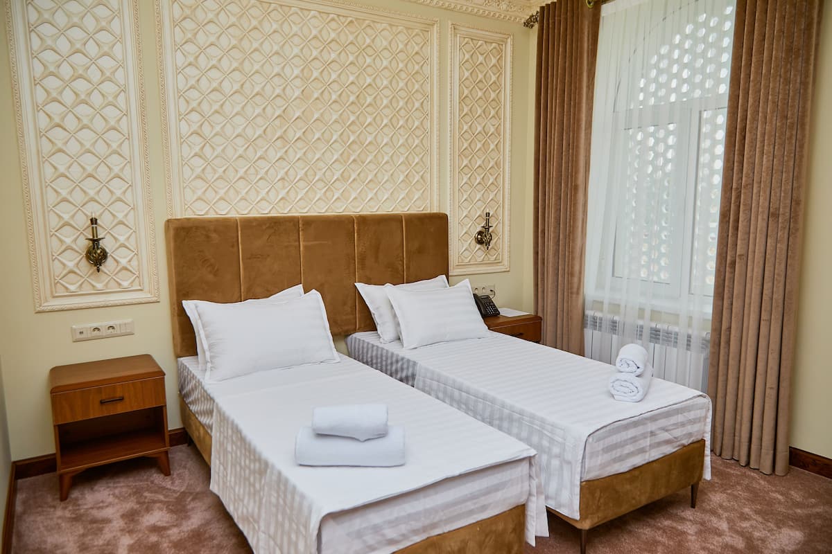 A hotel room with two beds, a nightstand, and a window with curtains.