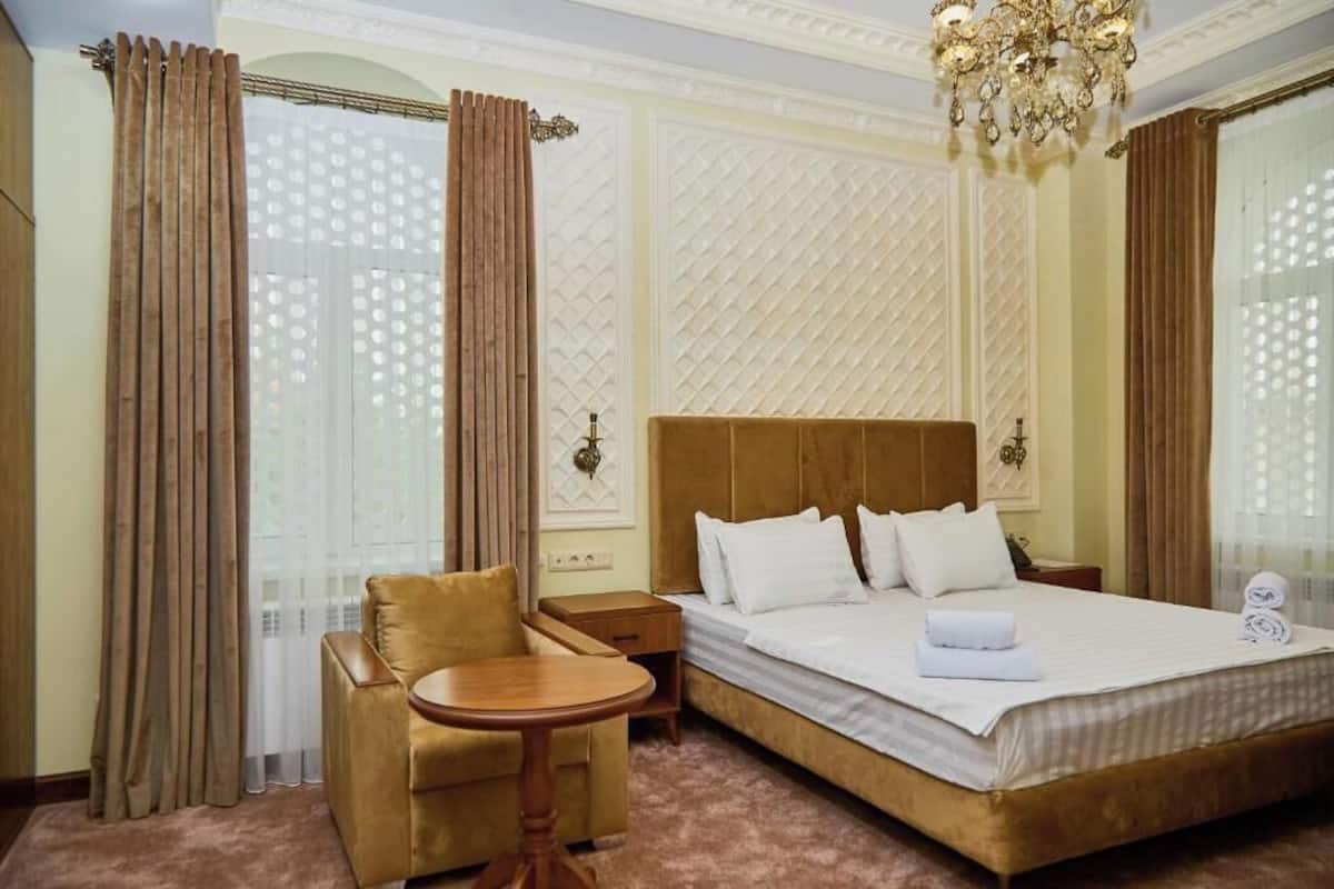 A hotel room with a large bed, a small round table, a sofa, and a chandelier.