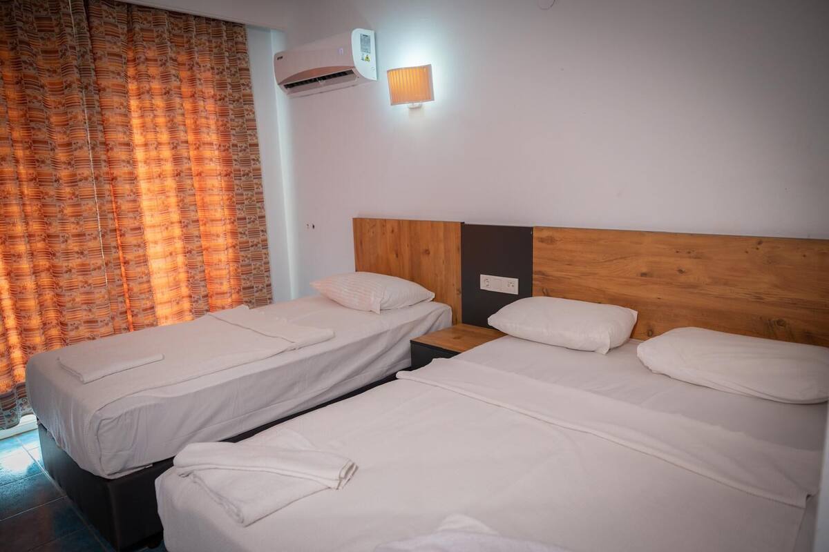 A hotel room with two single beds, a wooden headboard, an air conditioning unit, and a curtain with a floral pattern.