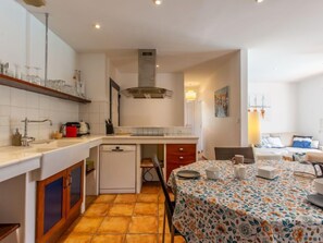 Uma cozinha compacta com lava-louças, um frigorífico pequeno e um espaço de refeições com toalha de mesa florida.