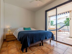 Quarto com cama, mesa de cabeceira, luminária e vista para área externa com rede e móveis de varanda.