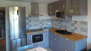 Una cocina compacta con refrigerador de acero inoxidable, microondas, horno empotrado y pileta.