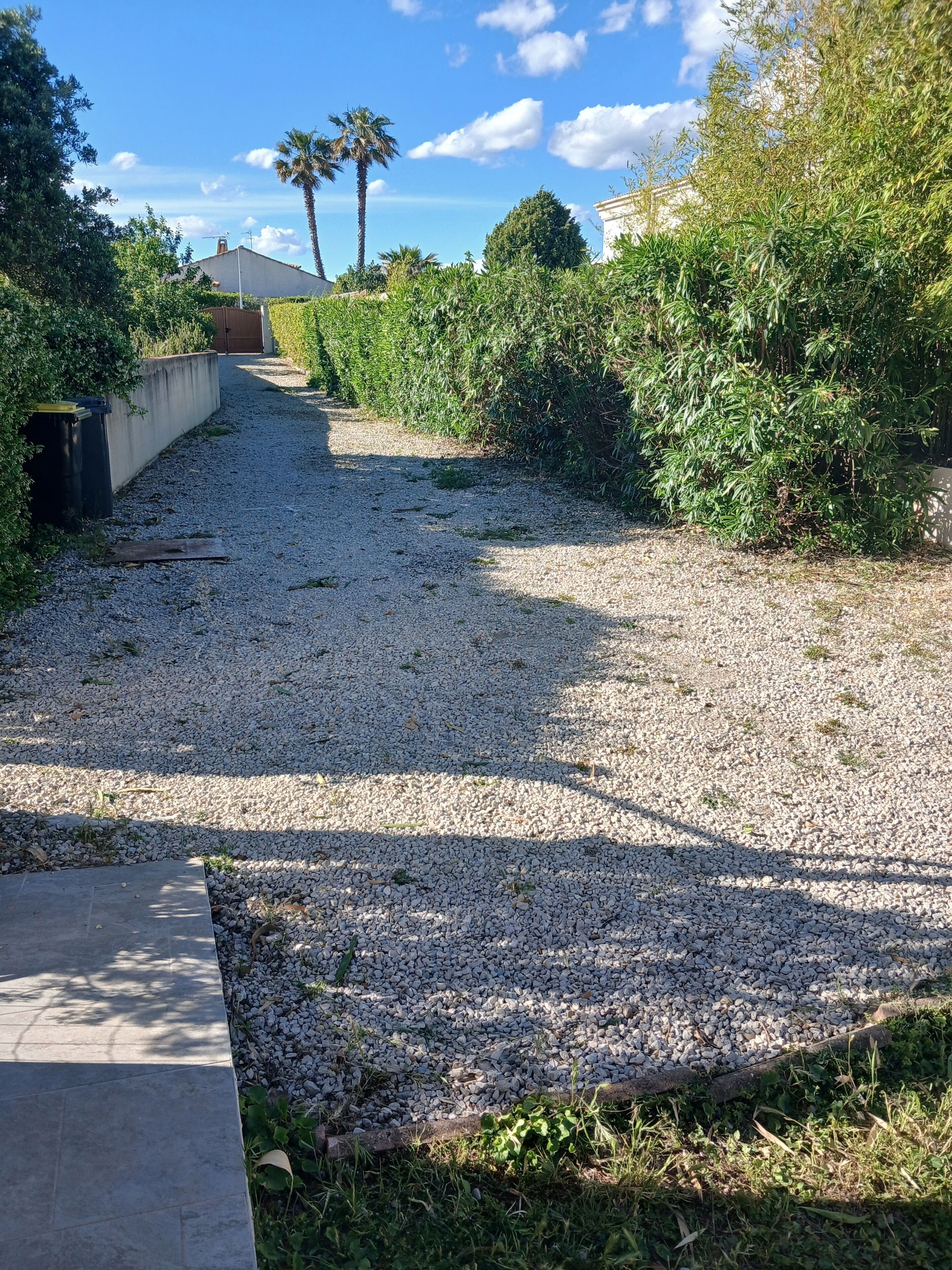 A gravel pathway leading to a building with a concrete wall and a door.