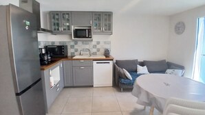 Una cocina compacta con refrigerador, microondas, cafetera y lavavajillas. Hay una pequeña mesa de comedor con sillas y un sofá con cojines.