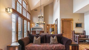 A spacious living room with a large brown sofa, wooden side tables, and a chandelier. - Catamount Lodge 408 Fabulous 2 Bedroom (Truckee)