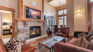 A cozy living room with a stone fireplace, comfortable seating, and a large window. - Catamount Lodge 408 Fabulous 2 Bedroom (Truckee)