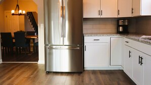 Eine Küche mit weißen Schränken, einem Edelstahl-Kühlschrank, einer Kaffeemaschine und einem Essbereich mit Stühlen und einem Tisch.