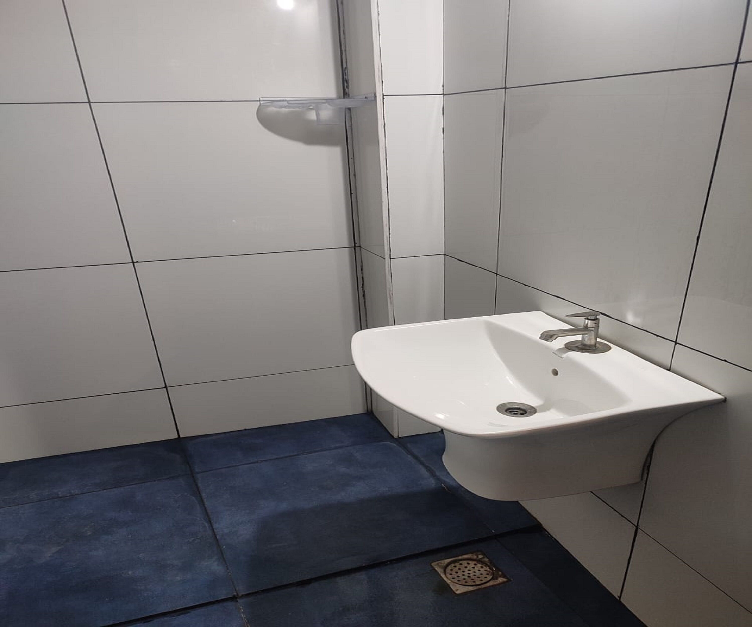 Un bagno con pareti piastrellate di bianco, un lavandino bianco con un rubinetto e un pavimento blu.