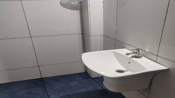 Un bagno con pareti piastrellate di bianco, un lavandino bianco con un rubinetto e un pavimento blu.