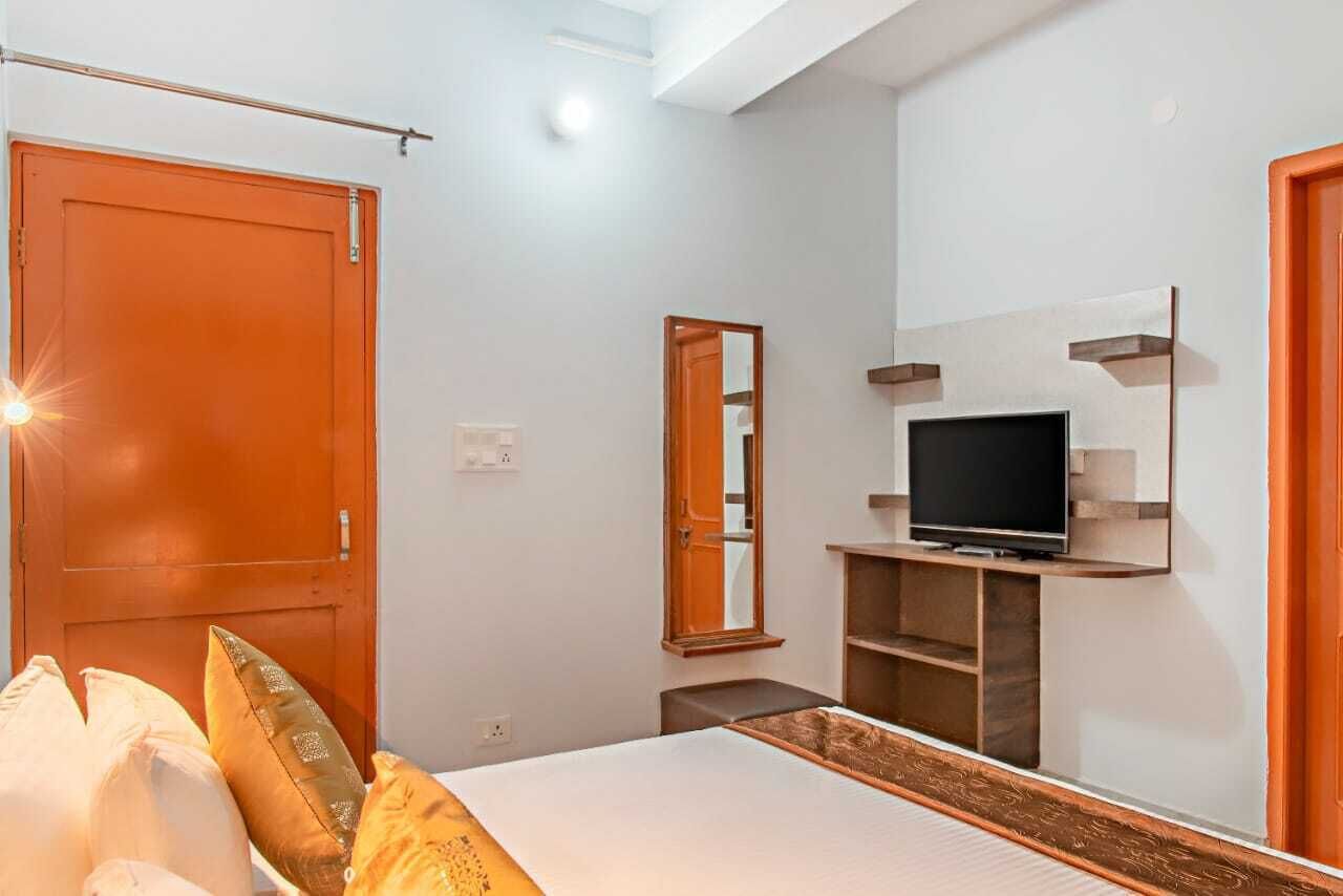 Quarto com cama, televisão sobre suporte de madeira, espelho e guarda-roupa.