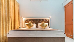 A large bed with a tufted headboard, two decorative pillows, and a bedside table with a bottle. - THE KASAULI TRAIL (Kasauli)