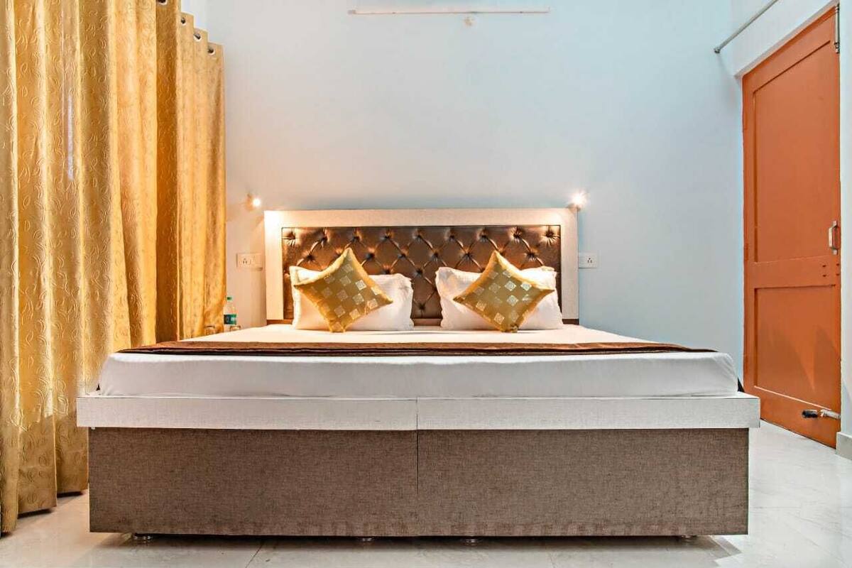 A large bed with a tufted headboard, two decorative pillows, and a bedside table with a bottle.