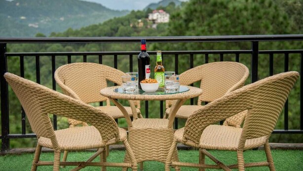 A wicker table set with chairs on a balcony with a scenic mountain view. - THE KASAULI TRAIL (Kasauli)