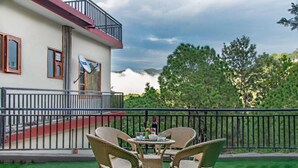 A two-story building with a balcony, wicker chairs, and a table set for dining. - THE KASAULI TRAIL (Kasauli)