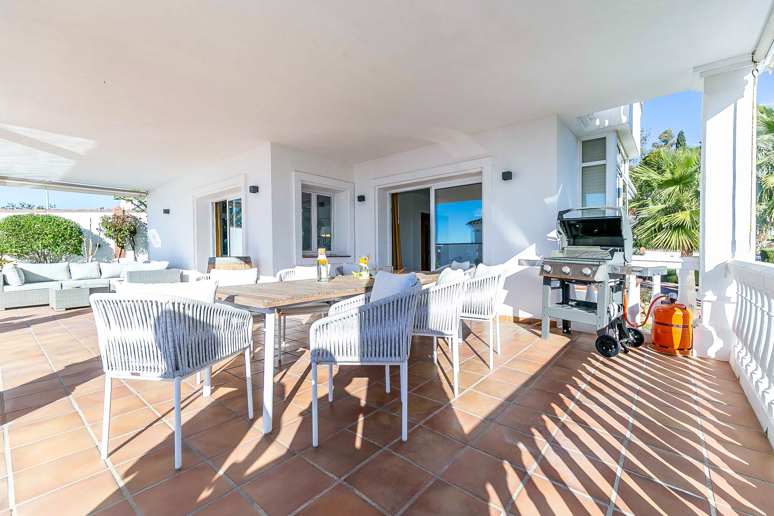 Una terrazza con mobili in vimini bianco, un barbecue e una bombola di gas.