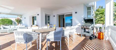 Una terrazza con mobili in vimini bianco, un barbecue e una bombola di gas.