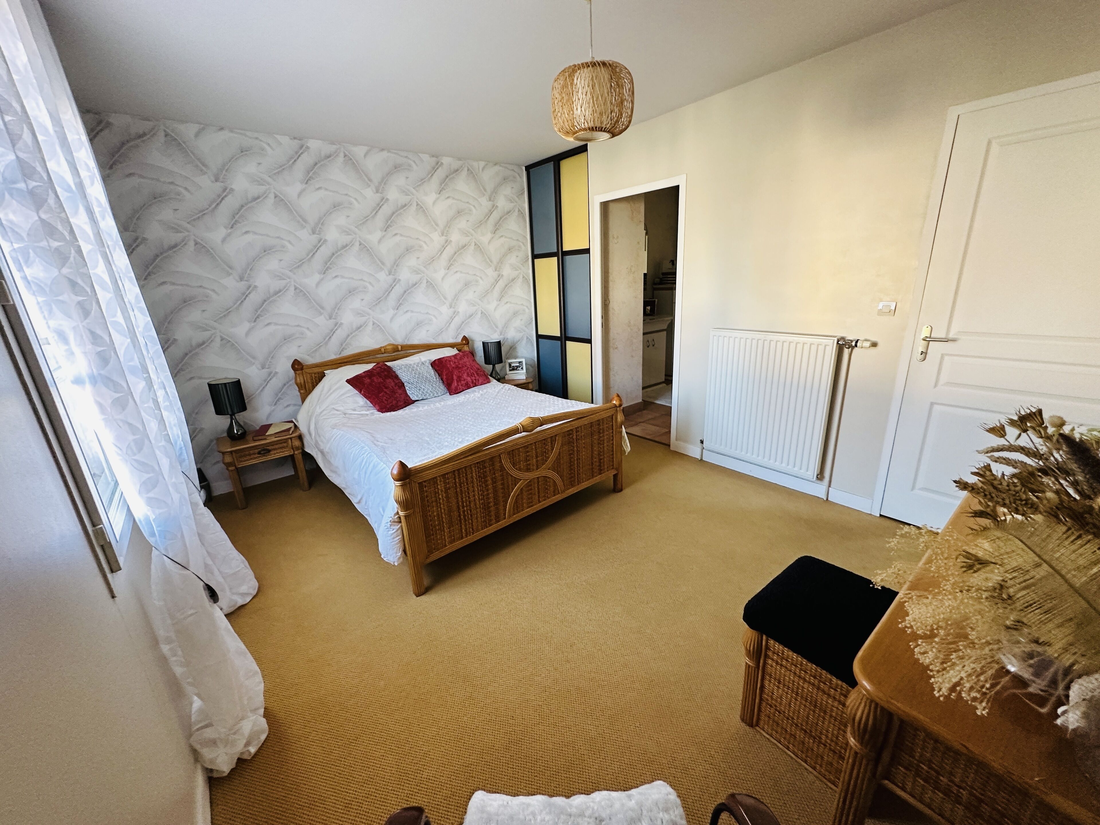 A bedroom with a bed, a nightstand, a lamp, a wicker chair, and a radiator.