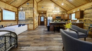 A log cabin interior with a large wooden-framed living room, a kitchen with wooden cabinets, a dining area, and a separate bathroom with a bathtub. - Moonlit Oaks Retreat | Romantic Broken Bow Cabin with Hot Tub, Fire Pit & Fireplace (Broken Bow)