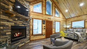 L’intérieur d’une cabane en rondins, avec une cheminée, un lit, un téléviseur et une fenêtre.
