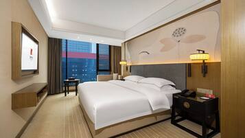 A hotel room with a large bed, bedside tables, a desk, and a view of a cityscape.