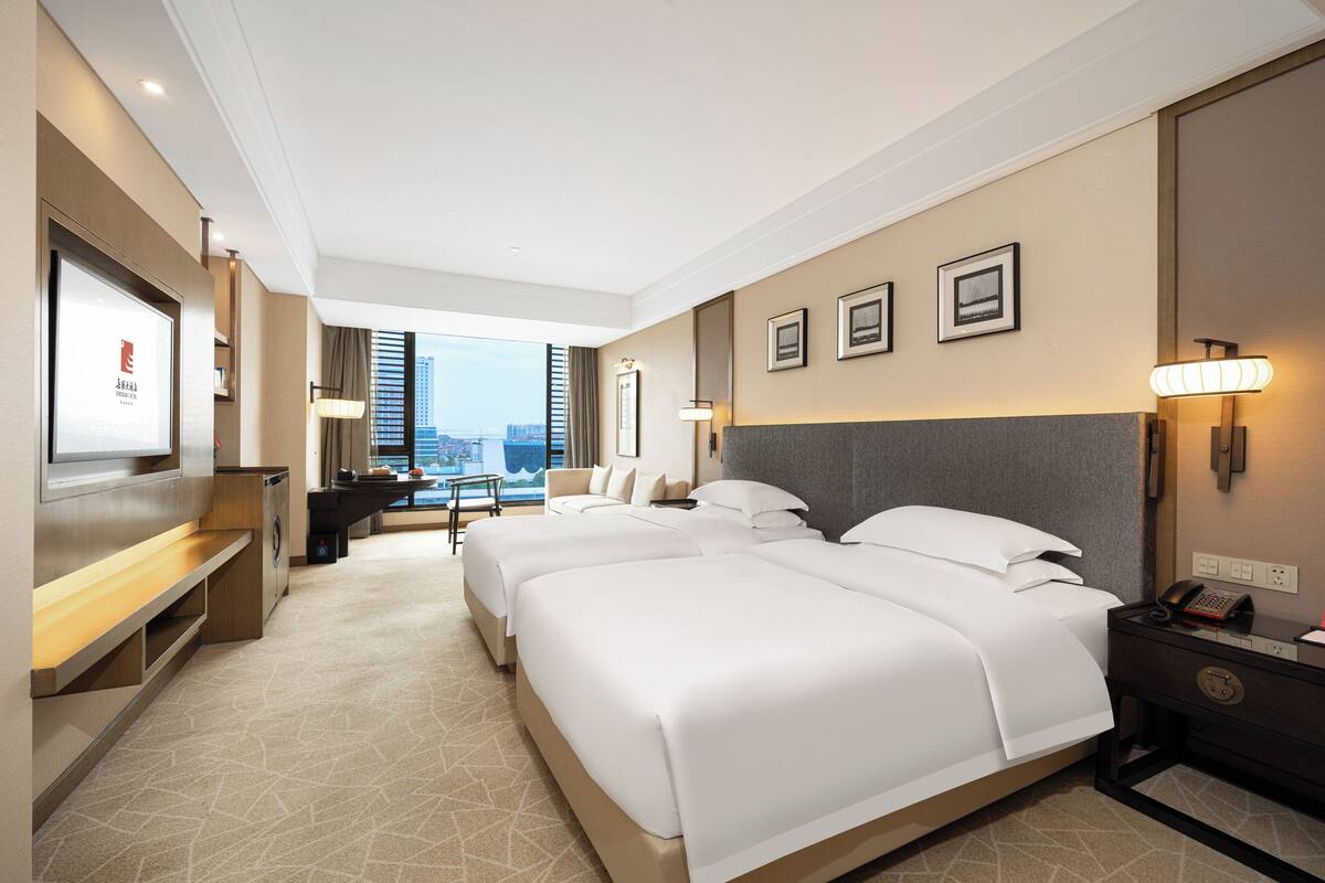 Ein Hotelzimmer mit einem großen Bett, einem Schreibtisch, einem Fernseher und Blick auf die Stadt.