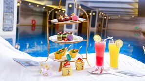 A tiered dessert stand with various pastries and macarons, a tray of colorful drinks, and a magazine on a white surface near a pool. - hunanyueyangHotel (Yueyang)