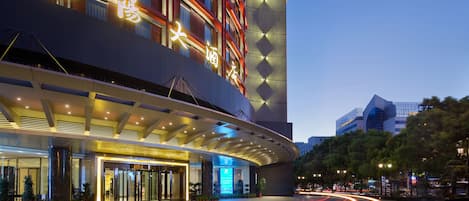 A modern hotel with illuminated signage, a curved entrance, and a well-lit facade.