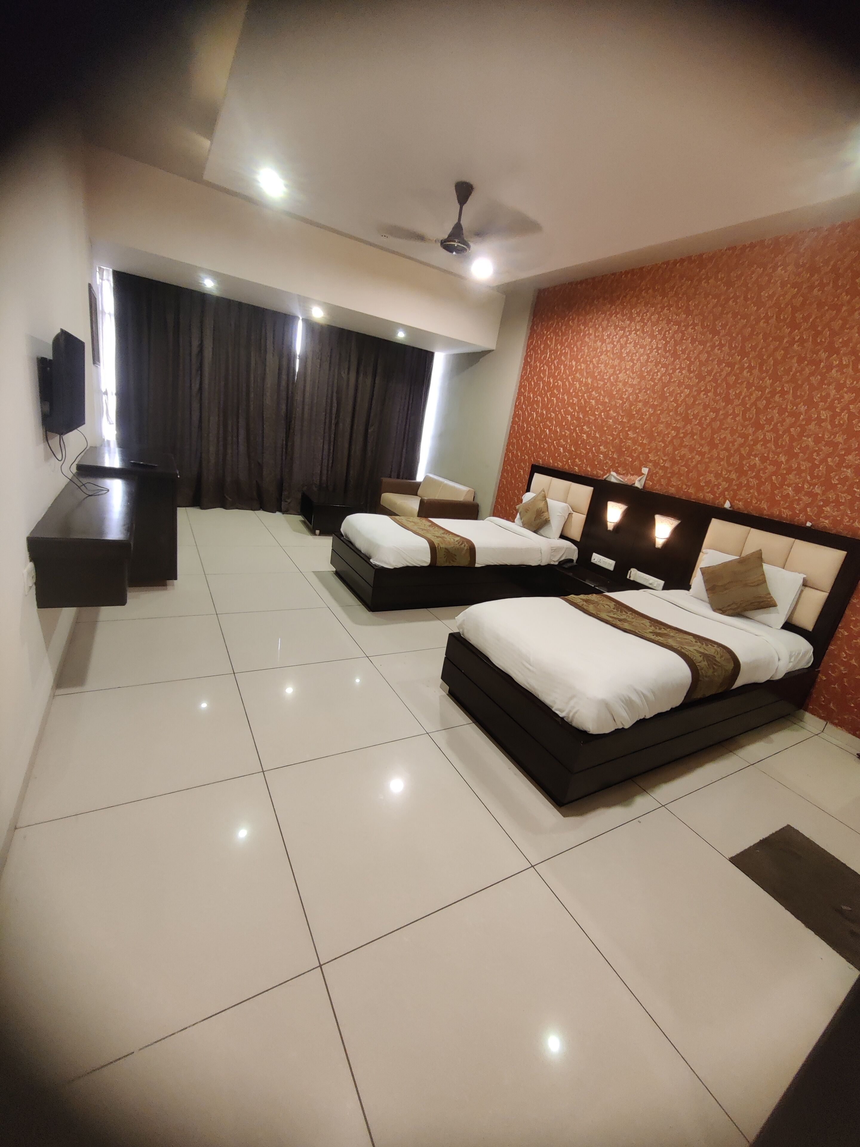 A hotel room with two beds, a TV, a ceiling fan, and a large window with curtains.