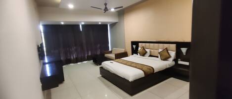 A modern bedroom with a large bed, a nightstand, a chair, a ceiling fan, and a view of the outside.