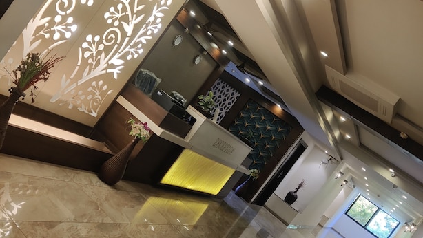 A modern reception area with a marble floor, a reception desk, decorative wall panels, and a seating area with cushions. - Hotel Restandview (Anand)