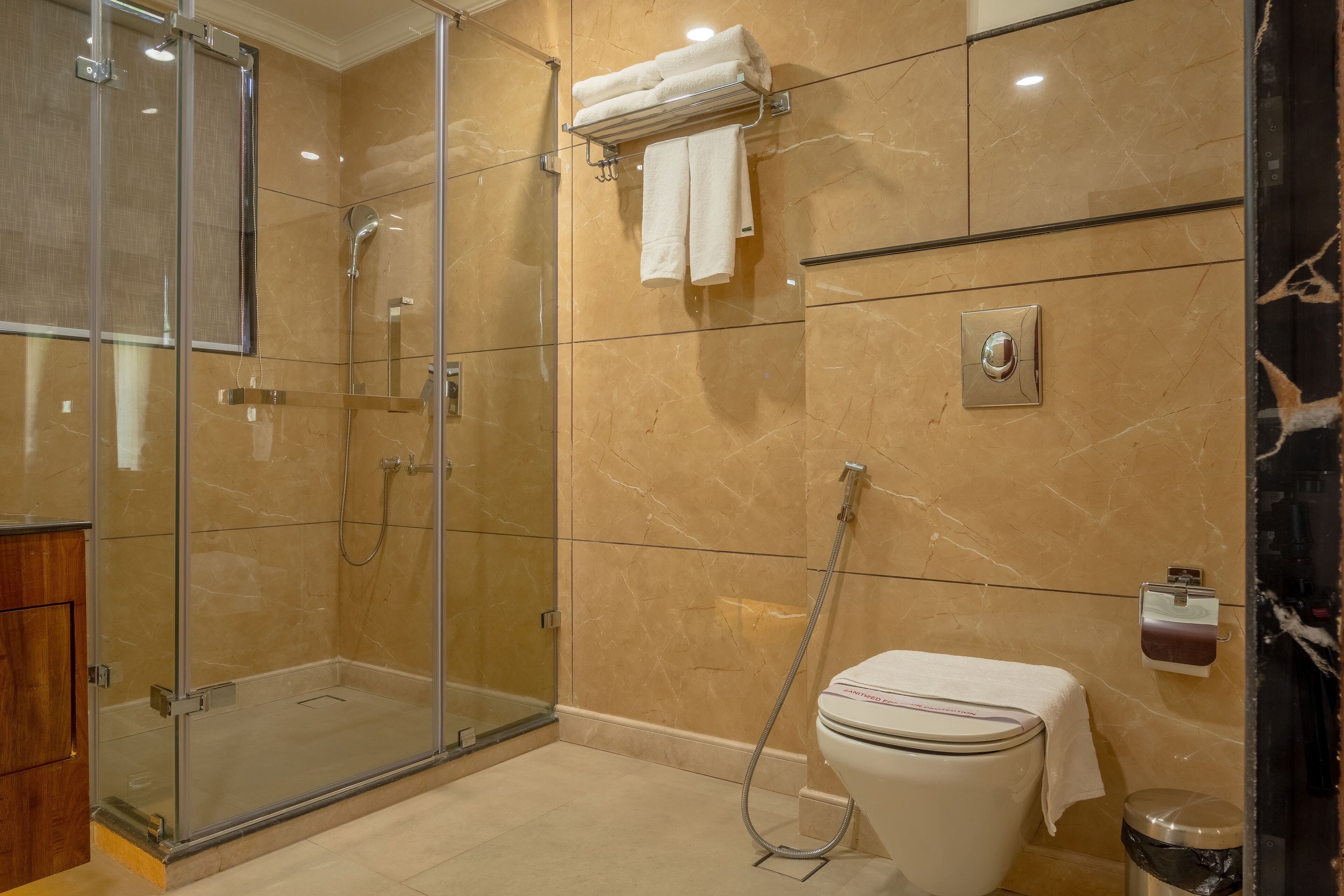 A modern bathroom with a glass-enclosed shower, a toilet with a towel on top, and a marble-tiled wall.