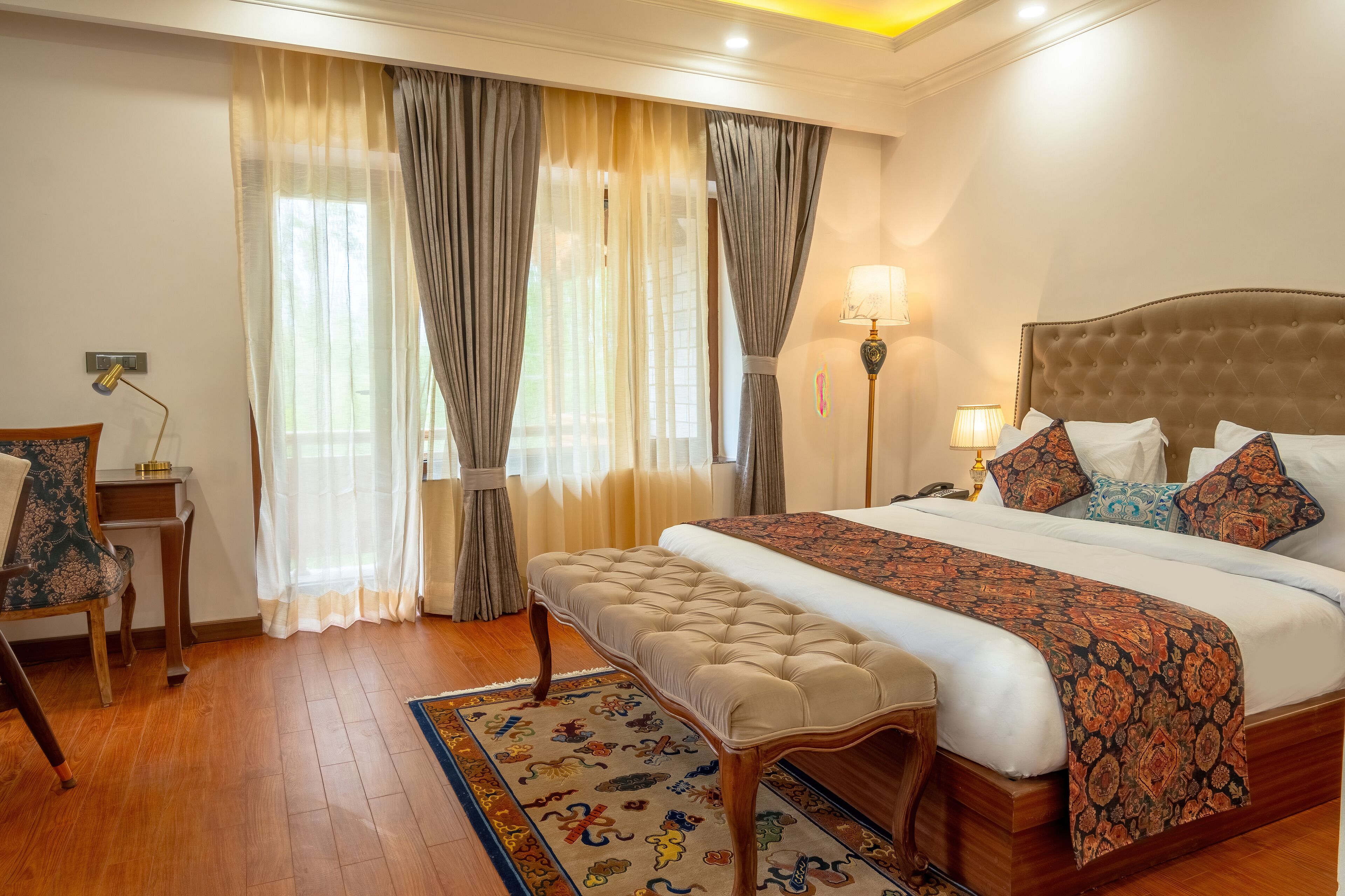 A hotel room with a large bed, a bench, a desk, and a chair.