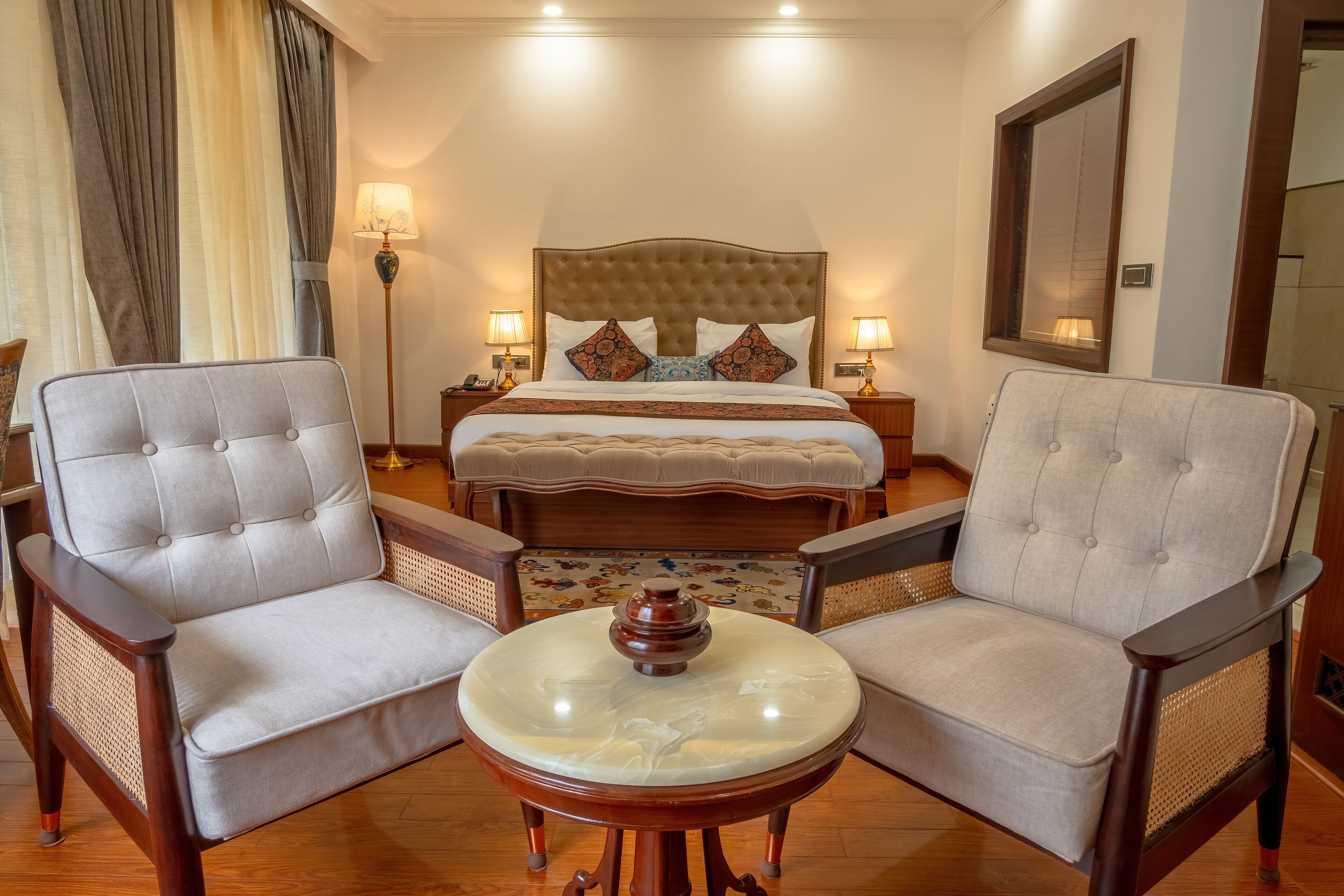 A hotel room with a large bed, two armchairs, a round coffee table, and a nightstand with lamps.
