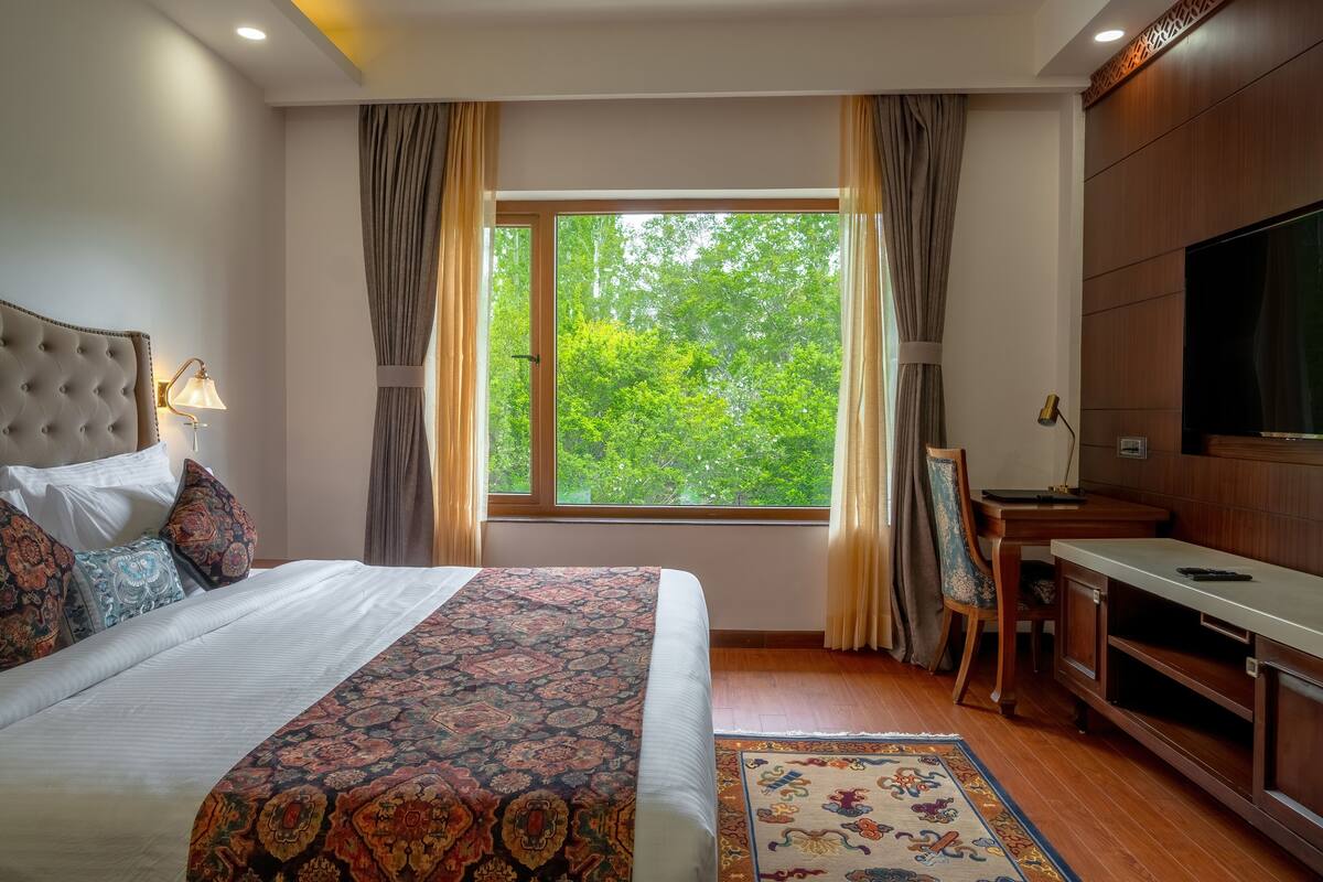 A hotel room with a large bed, a desk, a television, and a window with curtains.