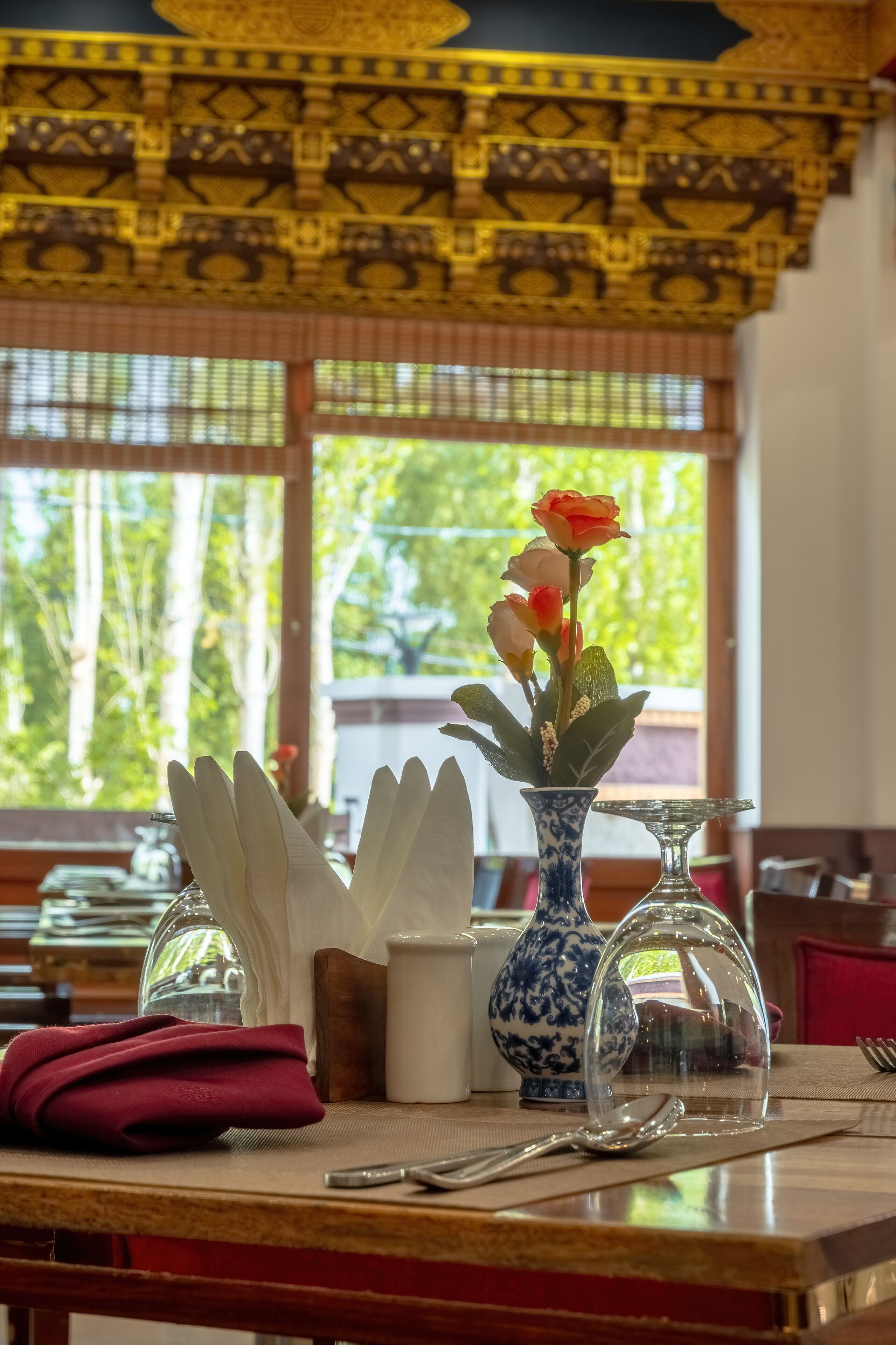 A dining table with a vase of flowers, a white napkin, a glass pitcher, and a spoon.