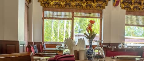Un comedor con mesas de madera y sillas rojas con acolchado, decorado con un florero y una jarra de vidrio.