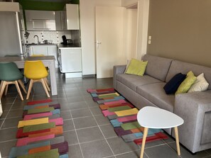 A modern apartment with a grey sofa, colorful rugs, and a small white table.