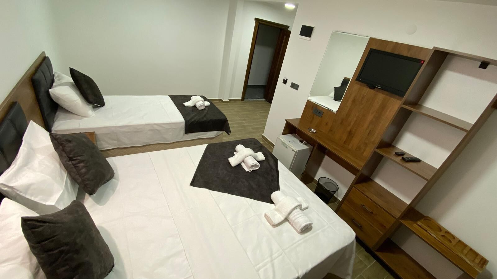 Habitación de hotel con dos camas, un armario de madera, un espejo y un escritorio pequeño.