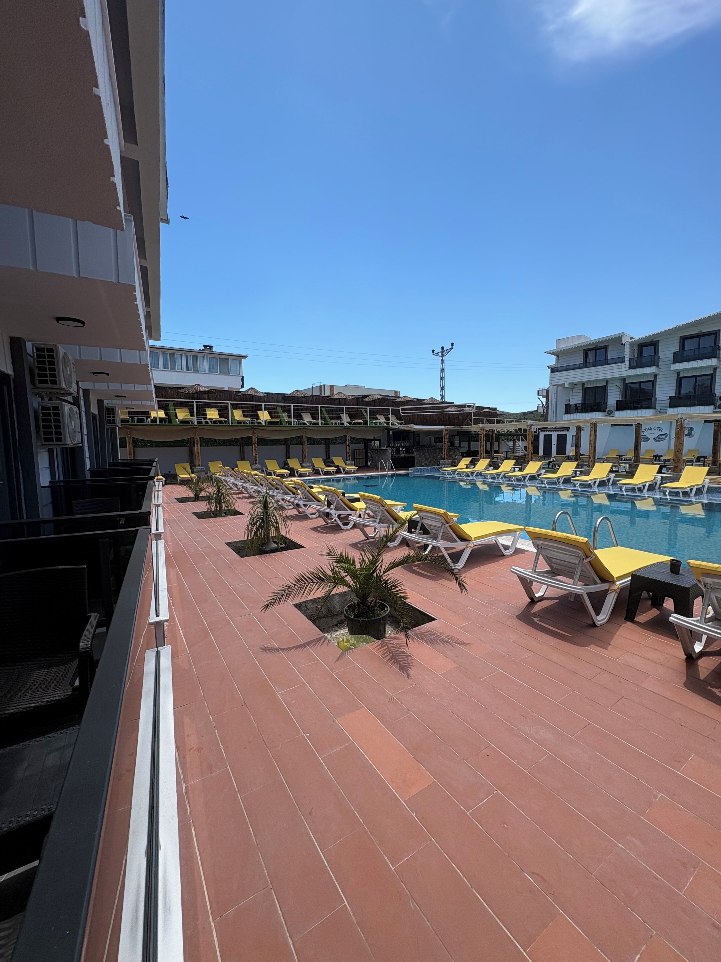 Un área de piscina en la azotea con sillas de descanso amarillas, una piscina y un edificio con varios balcones.