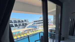 Ein Balkon mit Blick auf ein Schwimmbad, Liegestühle und ein Gebäude mit Wasserrutsche.