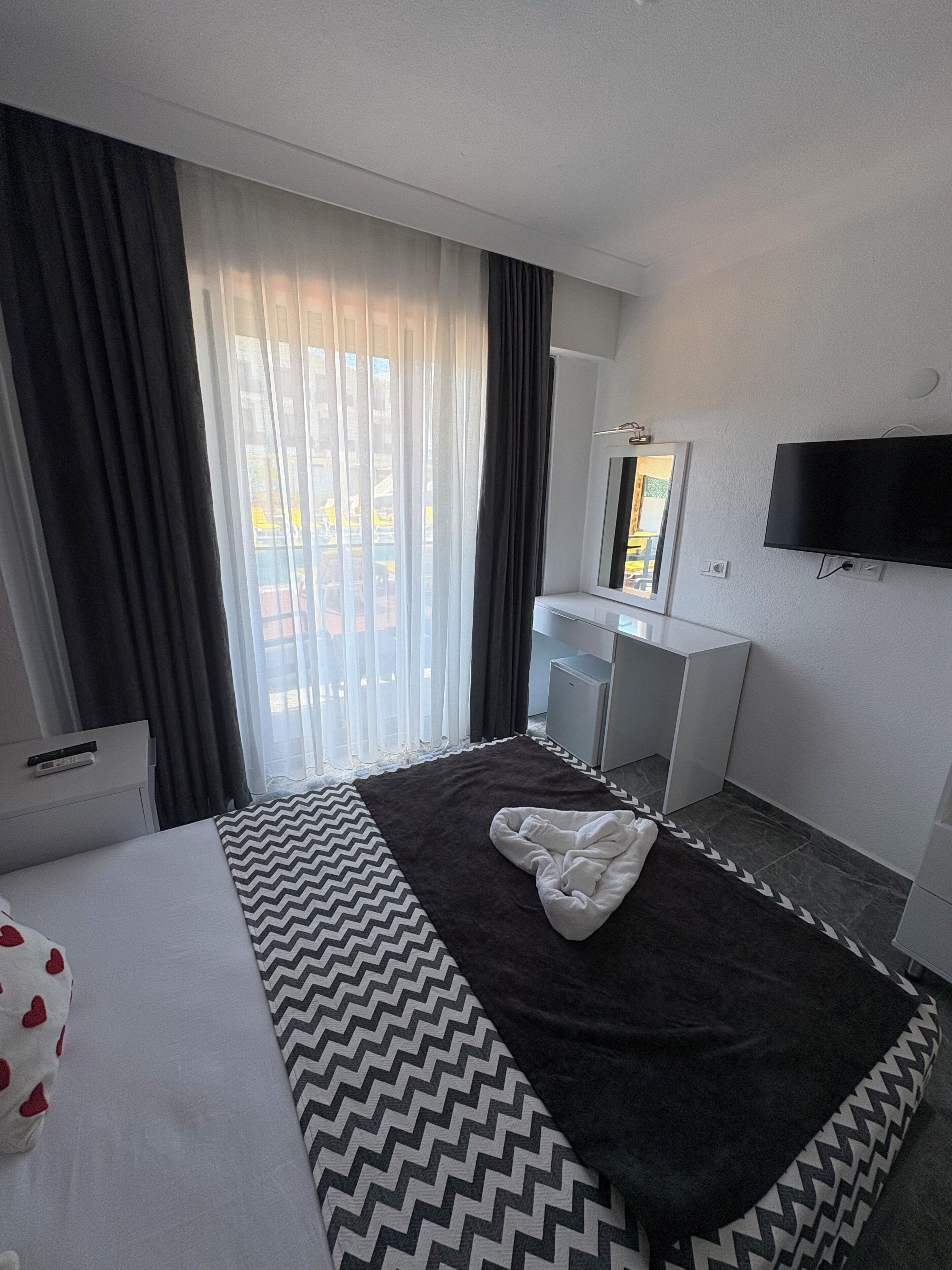 A hotel room with a bed, a desk, a television, and a window with curtains.