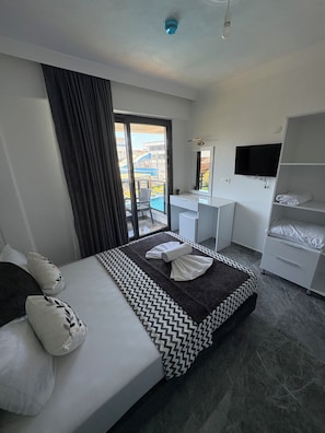 A modern hotel room with a bed, a desk, a TV, and a balcony with a view.