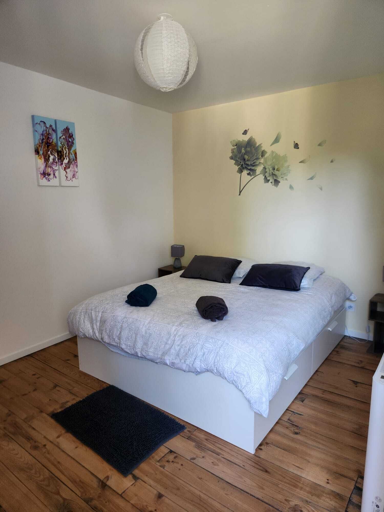 Quarto com cama, tapete, quadro na parede e luminária no teto.