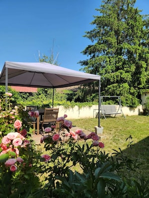 Un patio cubierto con una mesa y sillas, rodeado de exuberante vegetación y plantas con flores.